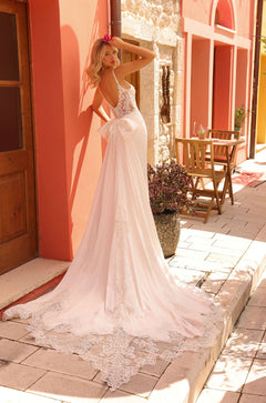 A bride in a lace wedding gown poses on a tiled patio with a pink wall, showcasing an elegant train.