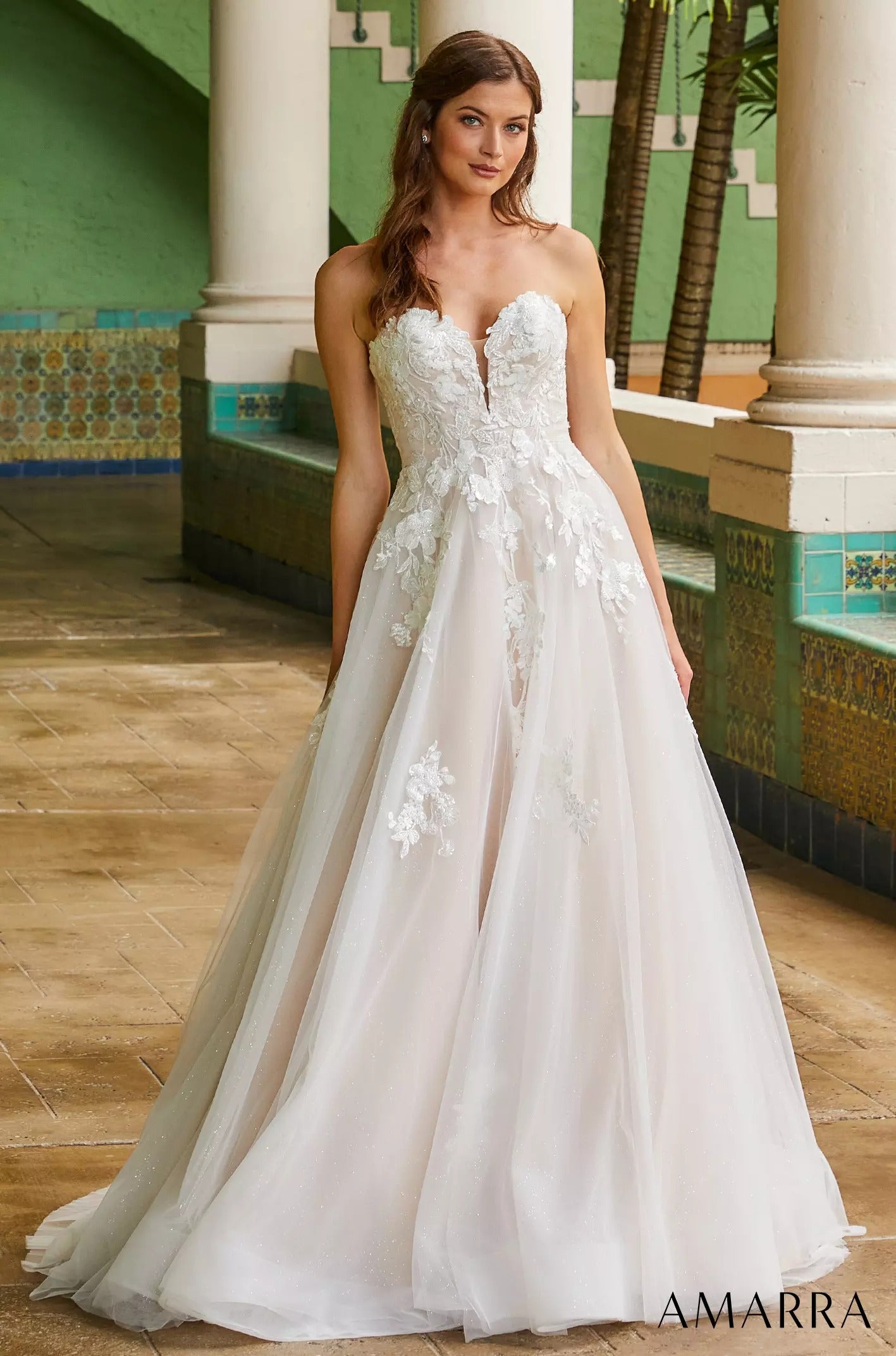 A white strapless ballgown wedding dress with floral lace appliqués, photographed in a tiled architectural setting.