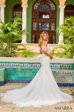 A bride in a white lace mermaid wedding gown poses before a green-walled, columned building with decorative tiles.