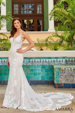 A bride in a lace mermaid wedding gown stands before a green building with decorative tiled walls.